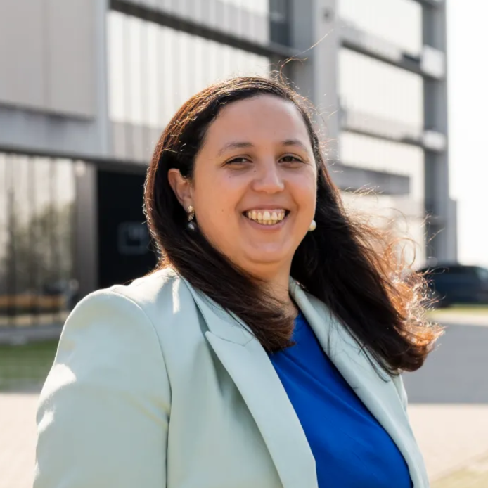 Lachende financieel adviseur Samra Daoud in mintgroene blazer voor modern kantoorgebouw.
